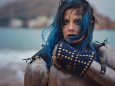 Medieval knight woman in armor prays, blessing before the battle. The Middle Ages history Fantasy photo. Beautiful female knight on the beach near mountains watching snow over sea