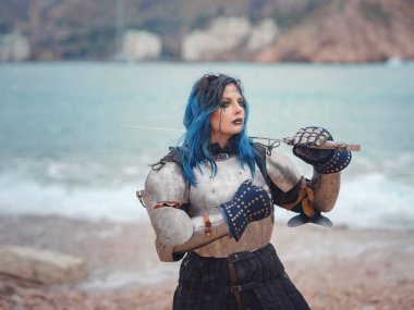 Medieval knight woman in armor prays, blessing before the battle. The Middle Ages history Fantasy photo. Beautiful female knight on the beach near mountains watching snow over sea