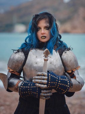 Medieval knight woman in armor prays, blessing before the battle. The Middle Ages history Fantasy photo. Beautiful female knight on the beach near mountains watching snow over sea