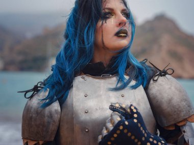 Medieval knight woman in armor prays, blessing before the battle. The Middle Ages history Fantasy photo. Beautiful female knight on the beach near mountains watching snow over sea