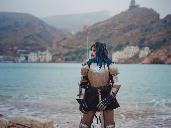 Ortaçağ şövalyesi kadın savaş öncesi dua ediyor. Orta Çağ tarihi fantezi fotoğrafı. Güzel bayan şövalye sahilde, dağların yakınında denizin üzerindeki karı seyrediyor.