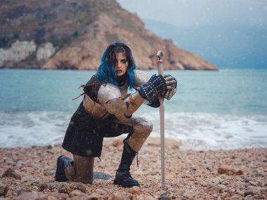 Medieval knight woman in armor prays, blessing before the battle. The Middle Ages history Fantasy photo. Beautiful female knight on the beach near mountains watching snow over sea