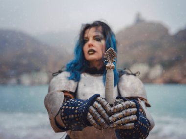 Medieval knight woman in armor prays, blessing before the battle. The Middle Ages history Fantasy photo. Beautiful female knight on the beach near mountains watching snow over sea