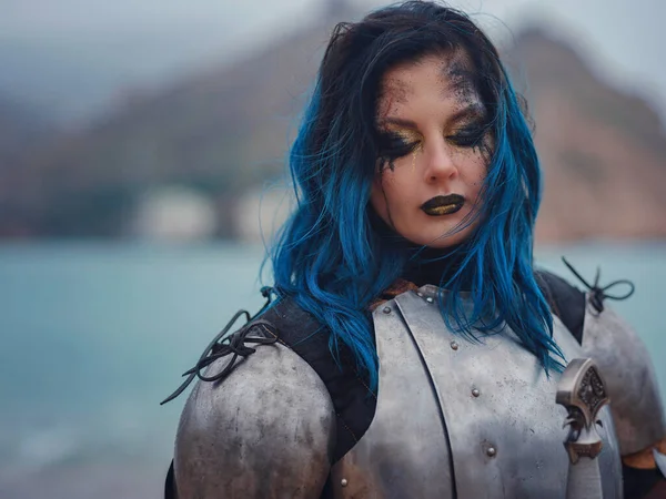 Ortaçağ şövalyesi kadın savaş öncesi dua ediyor. Orta Çağ tarihi fantezi fotoğrafı. Güzel bayan şövalye sahilde, dağların yakınında denizin üzerindeki karı seyrediyor.