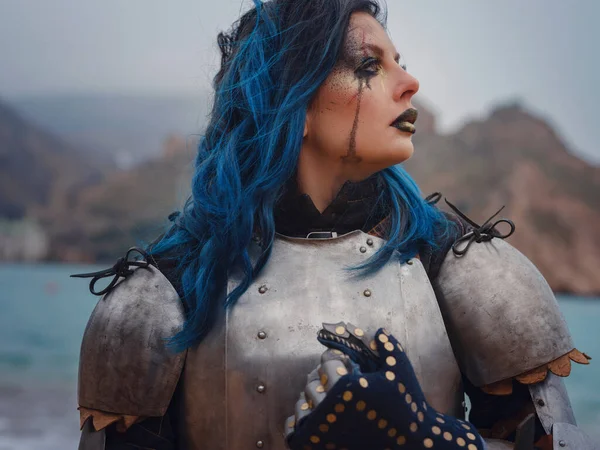 Ortaçağ şövalyesi kadın savaş öncesi dua ediyor. Orta Çağ tarihi fantezi fotoğrafı. Güzel bayan şövalye sahilde, dağların yakınında denizin üzerindeki karı seyrediyor.