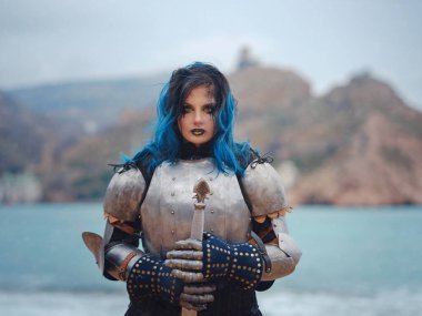 Medieval knight woman in armor prays, blessing before the battle. The Middle Ages history Fantasy photo. Beautiful female knight on the beach near mountains watching snow over sea