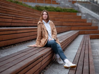 Güz bulutlu Moskova Zaryadye Parkı 'nda, güzel bej ceketli güzel bir kadın yürüyor. Sokak tarzı. Rusya 'ya Seyahat.