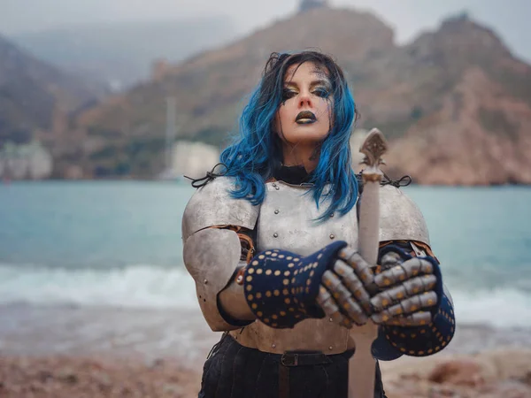 Medieval knight woman in armor prays, blessing before the battle. The Middle Ages history Fantasy photo. Beautiful female knight on the beach near mountains watching snow over sea