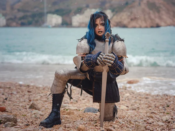 Medieval knight woman in armor prays, blessing before the battle. The Middle Ages history Fantasy photo. Beautiful female knight on the beach near mountains watching snow over sea