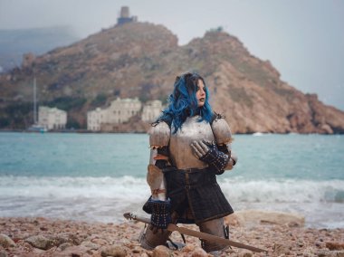 Medieval knight woman in armor prays, blessing before the battle. The Middle Ages history Fantasy photo. Beautiful female knight on the beach near mountains watching snow over sea