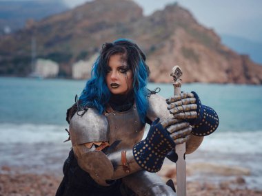 Medieval knight woman in armor prays, blessing before the battle. The Middle Ages history Fantasy photo. Beautiful female knight on the beach near mountains watching snow over sea