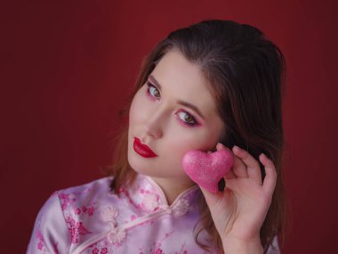 Çekici Asyalı kadının portresi. Elinde küçük parlak bir kalp tutuyordu. Kırmızı arka planda, geleneksel Çin elbisesi giymişti.