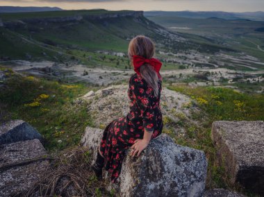 Boho 'lu kadın White Rock' ta güneşin doğuşunu seyrediyor. Kırmızı elbiseli güzel bir kadın. Kırsal kesimdeki çiftlikte yaşam tarzı açık hava portresi. Vahşi batı. Yaz tatili.
