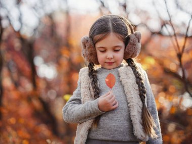 Portrait of small stylish beautiful model girl who stands in the autumn park at sunset. beautiful child in yellow autumn leaves.