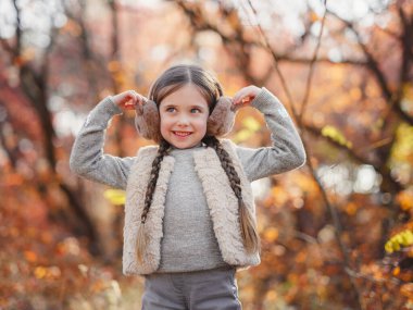 Portrait of small stylish beautiful model girl who stands in the autumn park at sunset. beautiful child in yellow autumn leaves.