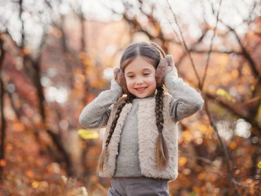 Portrait of small stylish beautiful model girl who stands in the autumn park at sunset. beautiful child in yellow autumn leaves.