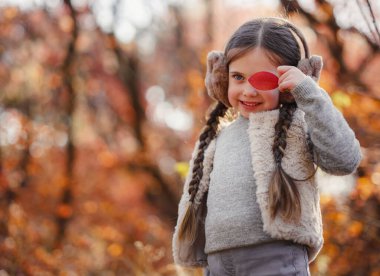 Portrait of small stylish beautiful model girl who stands in the autumn park at sunset. beautiful child in yellow autumn leaves.