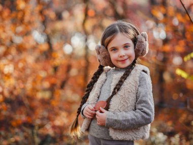 Portrait of small stylish beautiful model girl who stands in the autumn park at sunset. beautiful child in yellow autumn leaves.