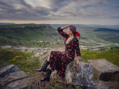 Boho 'lu kadın White Rock' ta güneşin doğuşunu seyrediyor. Kırmızı elbiseli güzel bir kadın. Kırsal kesimdeki çiftlikte yaşam tarzı açık hava portresi. Vahşi batı. Yaz tatili.