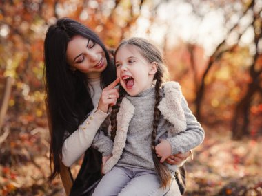 Fashionable mother with daughter. Family in a autumn park. spending weekend, picnic in autumn forest together. Mother and child relations.