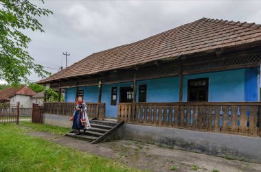 Salaj, Transilvanya, Romanya-16 Mayıs 2018: Romanya 'nın kırsal kesimindeki mavi bir evin önünde geleneksel Romen halk kostümü giyen yaşlı kadın