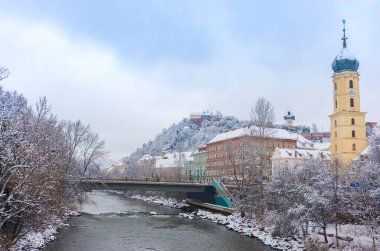 Mur nehri, Fransisken kilise kulesi ve arka plandaki ünlü saat kulesi, Graz, Steiermark, Avusturya şehir merkezinde, kışın karlı,