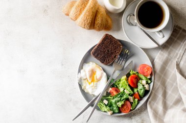 Sabah bahar sofrası dekorasyonu. Tabakta salata, yumurta, bir fincan kahve ve kruvasan, temiz beyaz masa örtüsünde vazoda taze laleler. Kahvaltı masası beyaz renkte ayarlanıyor.