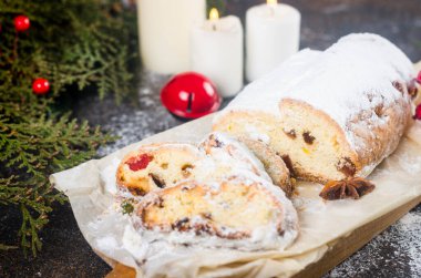Koyu ahşap masada, ksenli ağaç dalları ve süslemeleri olan kraft kağıdının üzerinde çalınmış. Yılbaşı Alman geleneksel meyveli ekmeği kurutulmuş böğürtlen, fındık ve pudra şekeriyle çalındı.. 