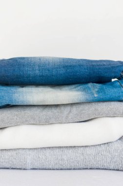 Gri arka planda kazak ve kot pantolon yığını, ütü, çamaşır, ev konforu, tekstil, örgü, kadın giysileri, pamuk, kadın günlük kıyafetleri beyaz, gri ve mavi