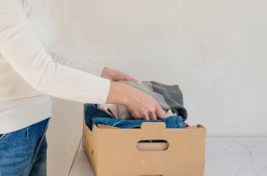 Kadın, karton kutuya giysiler koyar. İhtiyacımız olan bağışı yapar.