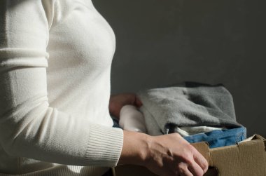 Kadın eşyaları karton kutuya koyuyor. Fakir insanlara bağışta bulun. Depolama konsepti yeniden kullanım, geri dönüşüm, yardım konsepti. Dünyadaki fakir insanlara yardım etmek için evde kullanılmış giysilerle dolu bir bağış kutusu..