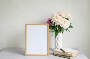 Vazodaki güzel beyaz şakayıklar ve boş ahşap çerçeve fotokopi alanı olan beyaz arka plandaki yazılar için kullanılıyor. Çiçek açan minimalist çiçeklerle dolu bir hayat.. 