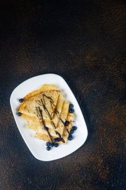 Ev yapımı krepler, koyu arkaplanda kahvaltı için gri tabakta çikolatalı ve dutlu lezzetli ince krepler. Geleneksel Rus mutfağı.