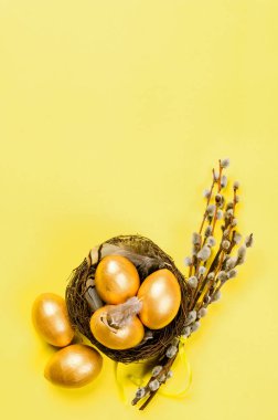 Yuvasında altın süslemeli yumurtalar ve altın arkaplanda tüyler olan bir yuva. Bahar tatili konsepti. Boşluğu kopyala, şablon modelleme Paskalya tebrik kartı ile metin için yer, 