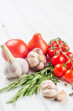 Organic red tomatoes cherry branch with green  rosemary,  garlic and spices on white old table. Ingredients for cooking. Clean eating concept. Vegetarian diet. 