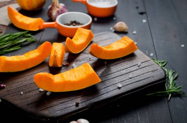 Kesme tahtasındaki çiğ balkabağı parçaları biberiye, tuz, baharat ve eski karanlık masa. Fırında pişirmek için sebze hazır. Sonbahar ev yemekleri