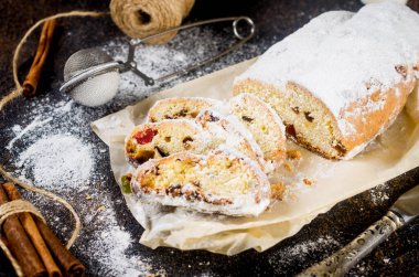 Koyu ahşap masada, ksenli ağaç dalları ve süslemeleri olan kraft kağıdının üzerinde çalınmış. Yılbaşı Alman geleneksel meyveli ekmeği kurutulmuş böğürtlen, fındık ve pudra şekeriyle çalındı.. 