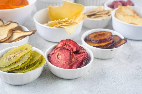 assortied dried chips and ripe fruits in plates on grey background. Fruit chips. Healthy eating concept, snack, no sugar. Top view, copy space.