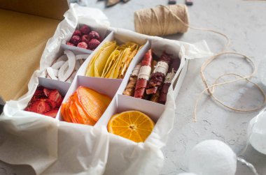 Gri arka plandaki kutuda çeşitli el yapımı organik kurutulmuş cips. Sağlıklı beslenme konsepti, atıştırmalık, şekersiz. Bakım paketi, mevsimlik hediye kutusu. Noel tatili için çevre dostu sepetler.