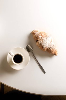Freshly baked French croissant for breakfast on plate and cup of hot coffee on white table. Tasty croissants.