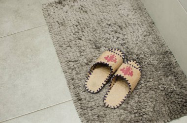 Pair ladies slippers over soft grey carpet on floor near tub in bathroom. Concept of cleanliness and personal care, top view