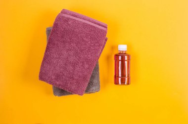 Katlanmış gri ve mor havlular, sarı arka planda bir şişe şampuan ve mor duş jeli. Kopya alanı ile banyo maketi.