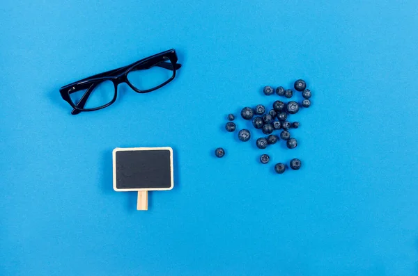 Glasses and fresh blueberries on blue background. Natural products to improve vision. Concept for healthy eating and vision.