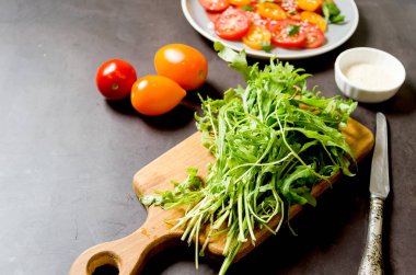 Fresh arugula on cutting board with tomatoes. ingredients for cooking fresh healthy vegetable salad. Summer food concept. Selective focus