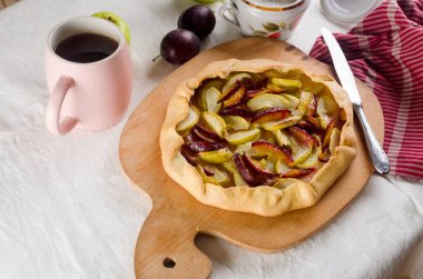 Beyaz keten masa örtüsü üzerinde elma ve erikli ev yapımı galet. Açık turta. Masadaki ev yapımı turta kabuğunun en üst görüntüsü. Kırsal ev yapımı meyveli turta..