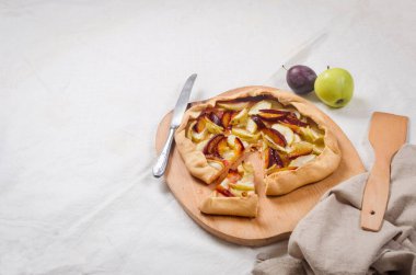 Beyaz keten masa örtüsü üzerinde elma ve erikli ev yapımı galet. Açık turta. Masadaki ev yapımı turta kabuğunun en üst görüntüsü. Kırsal ev yapımı meyveli turta..