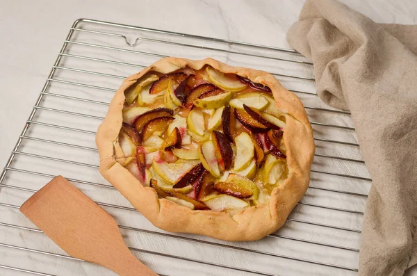 Homemade galette with apple and plum on a white linen tablecloth. Open pie. Top view of homemade pie crust on the table. rustic home baked fruit pie.