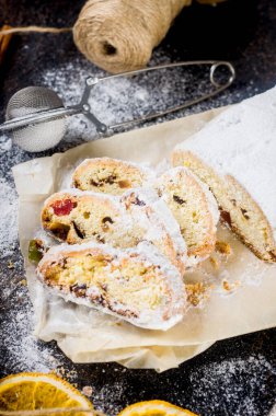 Koyu ahşap masada, ksenli ağaç dalları ve süslemeleri olan kraft kağıdının üzerinde çalınmış. Yılbaşı Alman geleneksel meyveli ekmeği kurutulmuş böğürtlen, fındık ve pudra şekeriyle çalındı.. 