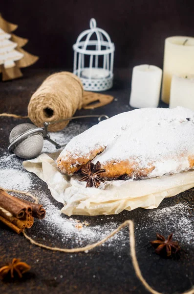 Stollen sliced on kraft paper on dark wooden table with xmas tree branches and decorations,. Christmas German traditional fruit bread stollen with dried berries, nuts and powdered sugar.