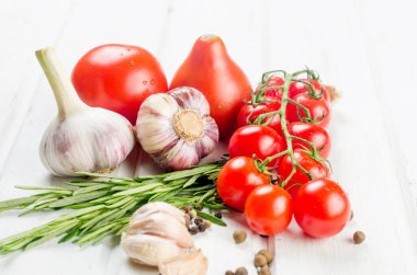 Organic red tomatoes cherry branch with green  rosemary,  garlic and spices on white old table. Ingredients for cooking. Clean eating concept. Vegetarian diet. 